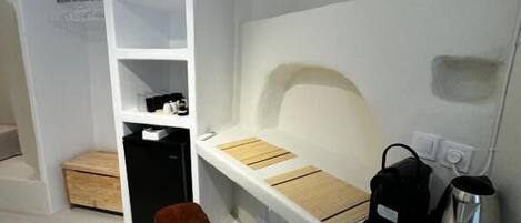 Una habitación moderna y minimalista con un escritorio blanco, dos sillas marrones, un bolso negro y un hervidor plateado.