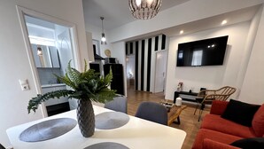 Un moderno salón con una mesa de comedor blanca, un sofá rojo y un televisor montado en la pared.
