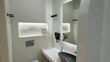 Une salle de bain moderne avec des toilettes blanches, un lavabo rond doté d’un plan de toilette en bois, et un miroir au-dessus du lavabo.