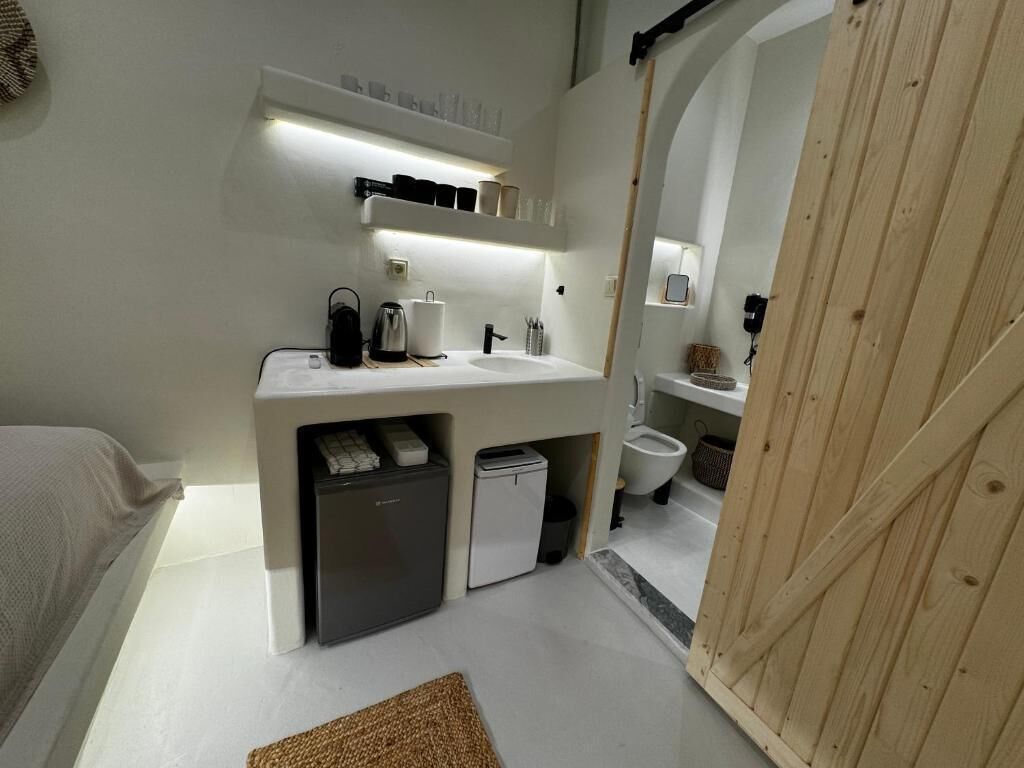 Ein kleines, modernes Badezimmer mit integriertem Waschbecken, einer kleinen Kühlbox und einer Toilette.