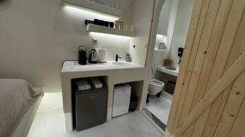 Ein kleines, modernes Badezimmer mit integriertem Waschbecken, einer kleinen Kühlbox und einer Toilette.