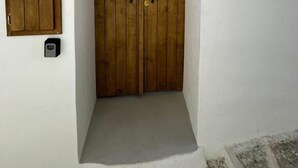 Un edificio blanco con una puerta doble de madera y un pequeño armario de madera a la izquierda.
