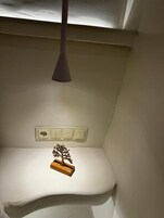 Una esquina de una habitación con un estante blanco, una pequeña decoración de árbol de madera y una lámpara colgante.