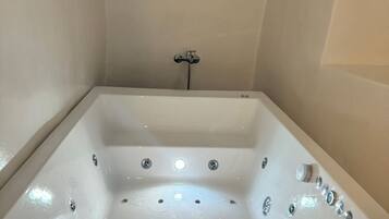 A large, rectangular bathtub with multiple faucets and a control panel, set in a room with plain walls and a light-colored floor.