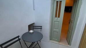 Un pequeño espacio al aire libre con mesa y sillas, un banco y una puerta que da a un área interior.