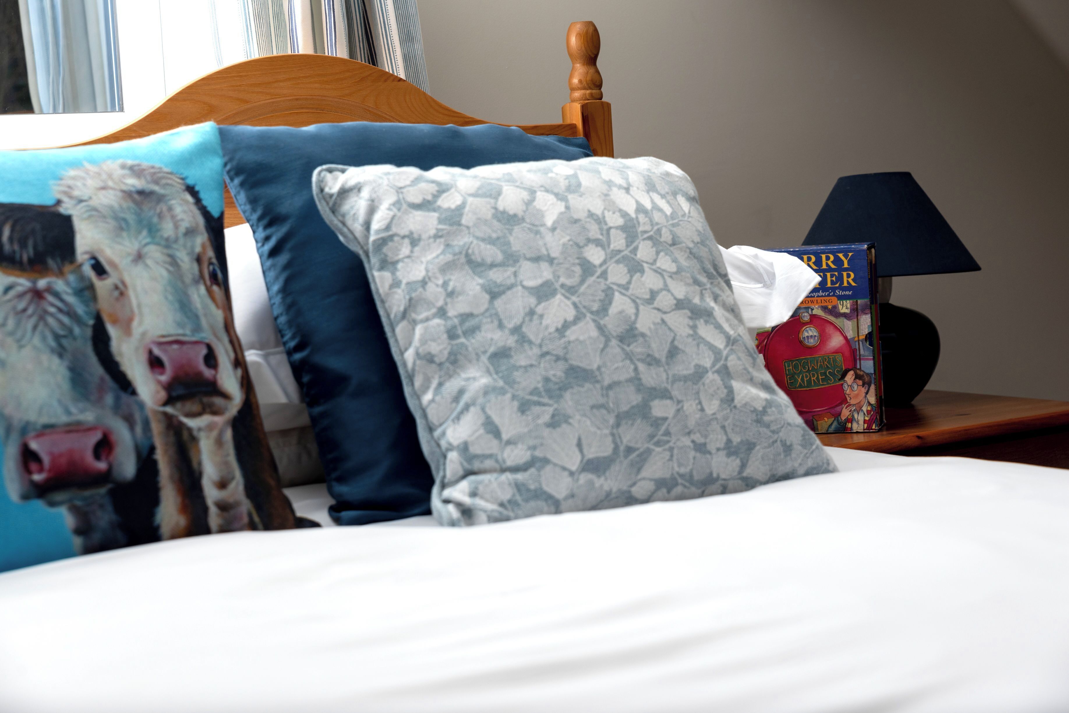 A bed with a wooden headboard, blue and patterned pillows, a book titled "Hogwarts Express," and a lamp on a bedside table.