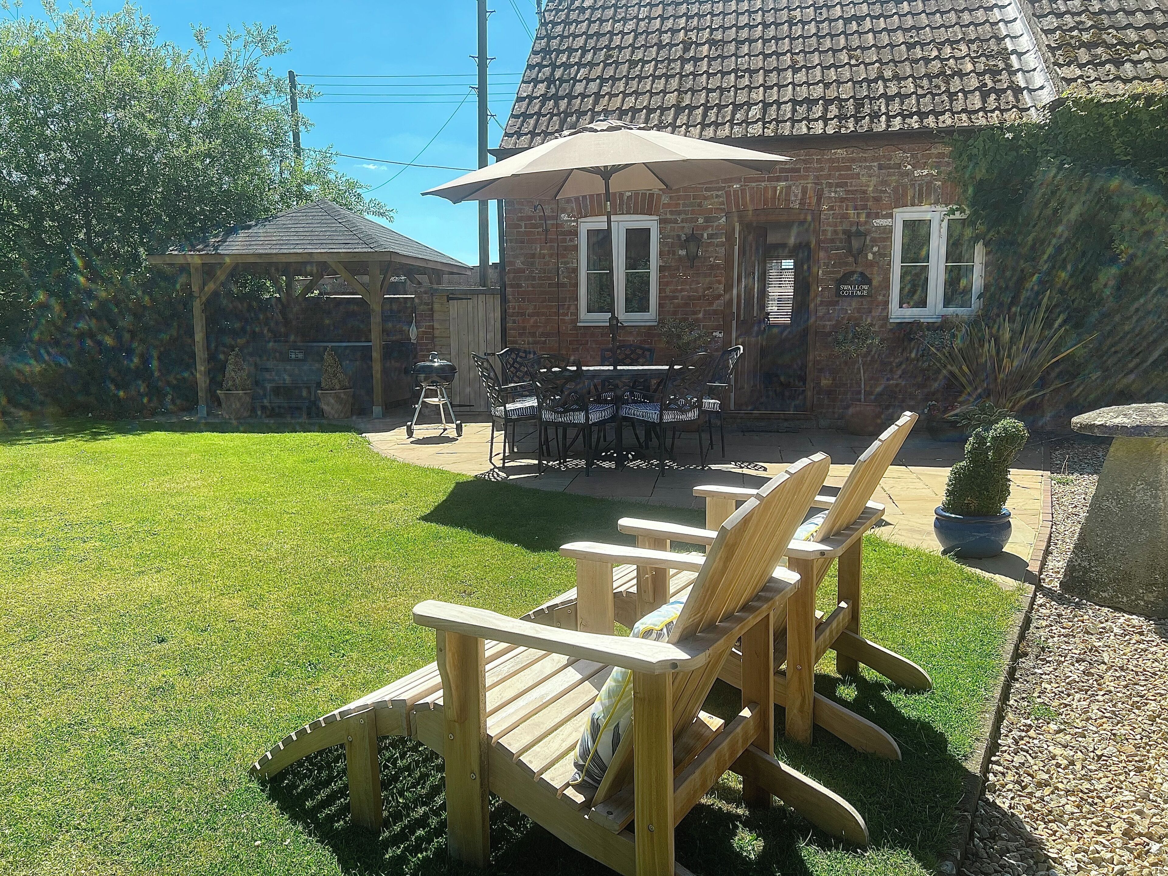 Un jardin avec un espace barbecue, des sièges d’extérieur et une maison avec un toit en tuiles.