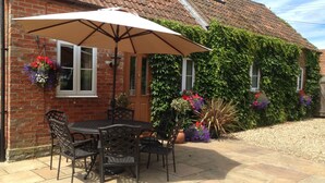 A patio with a table and chairs, a large umbrella, and potted plants. - Swallow Cottage @ Olivemead Farm (Chippenham)