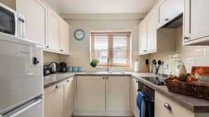 A kitchen with white cabinets, a microwave, a sink, and a clock on the wall. - Swallow Cottage @ Olivemead Farm (Chippenham)