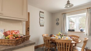 A dining area with a wooden table, chairs, a basket of fruits, and a breakfast setting. - Swallow Cottage @ Olivemead Farm (Chippenham)