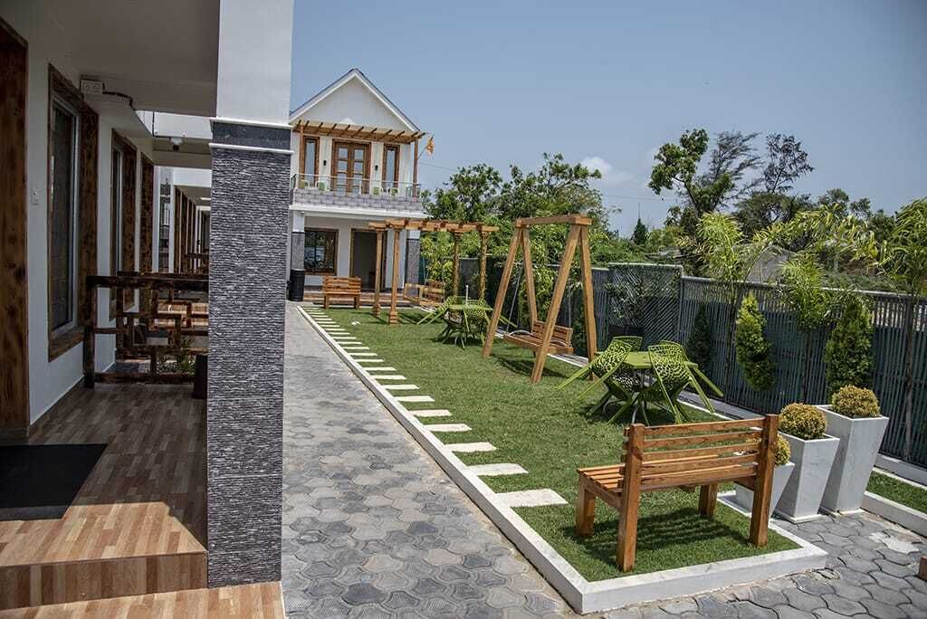 Una casa moderna con un patio que cuenta con un conjunto de columpio de madera, un pequeño jardín y un camino que lleva a la entrada.