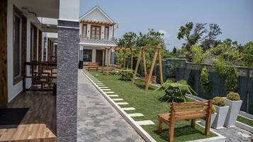 Una casa moderna con un patio que cuenta con un conjunto de columpio de madera, un pequeño jardín y un camino que lleva a la entrada.