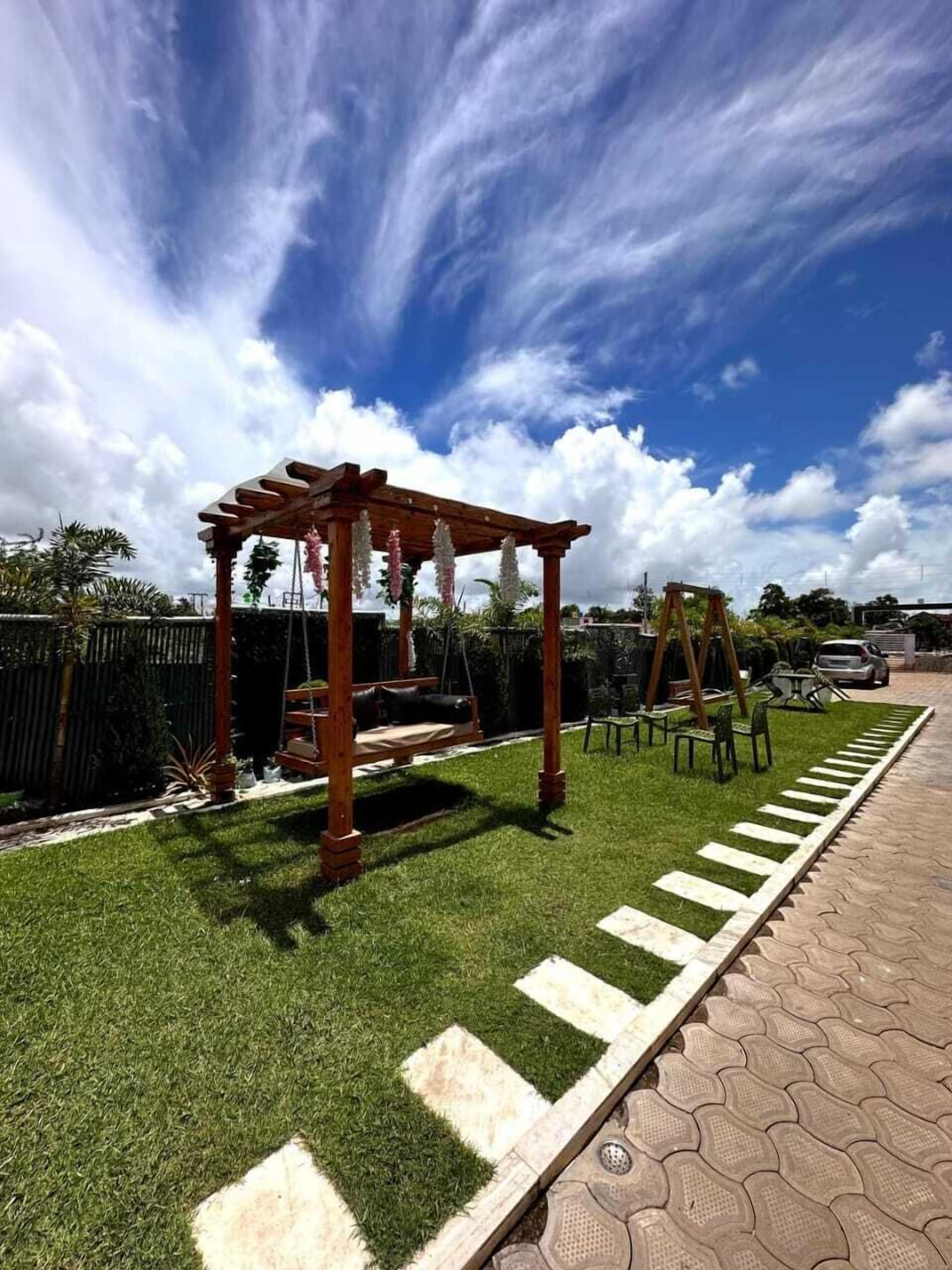 A wooden swing set and a small table in a grassy area with a paved path.