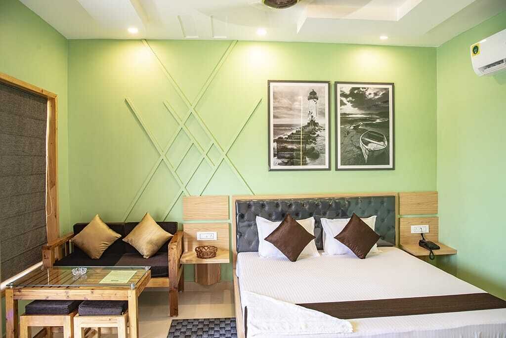 A hotel room with a bed, a sofa, a small table, and two framed pictures on the wall.