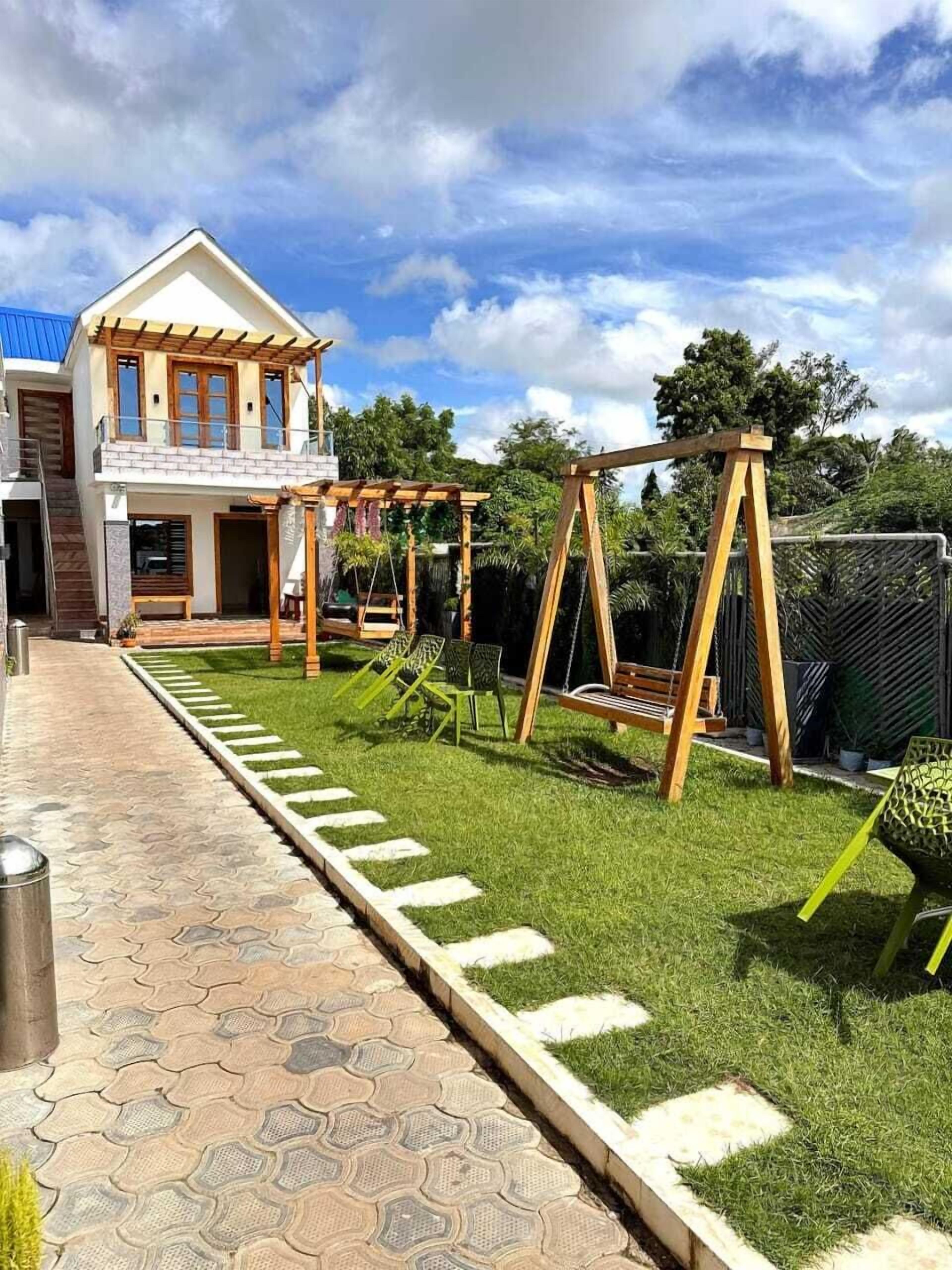 Una casa de dos pisos con balcón, un camino empedrado y un jardín con columpios.