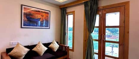 Una habitación con un sofá de madera, un ventilador de techo, un cuadro enmarcado y vistas a través de un ventanal.