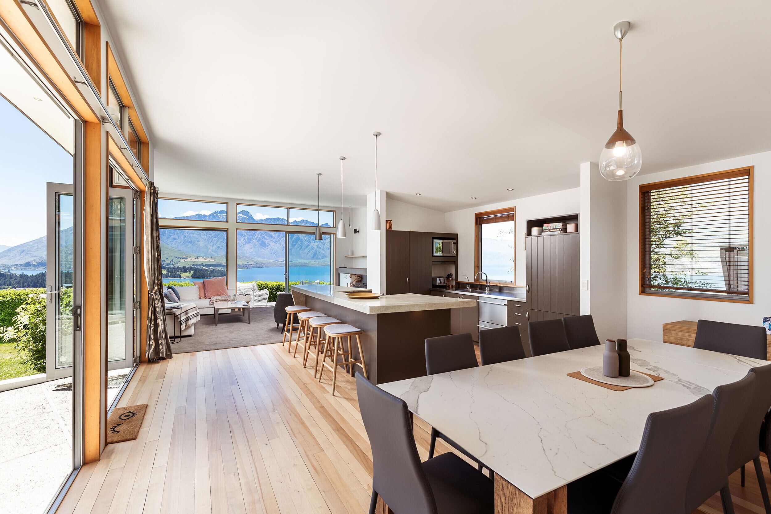A modern kitchen with a large island, dining area, and a view of mountains.