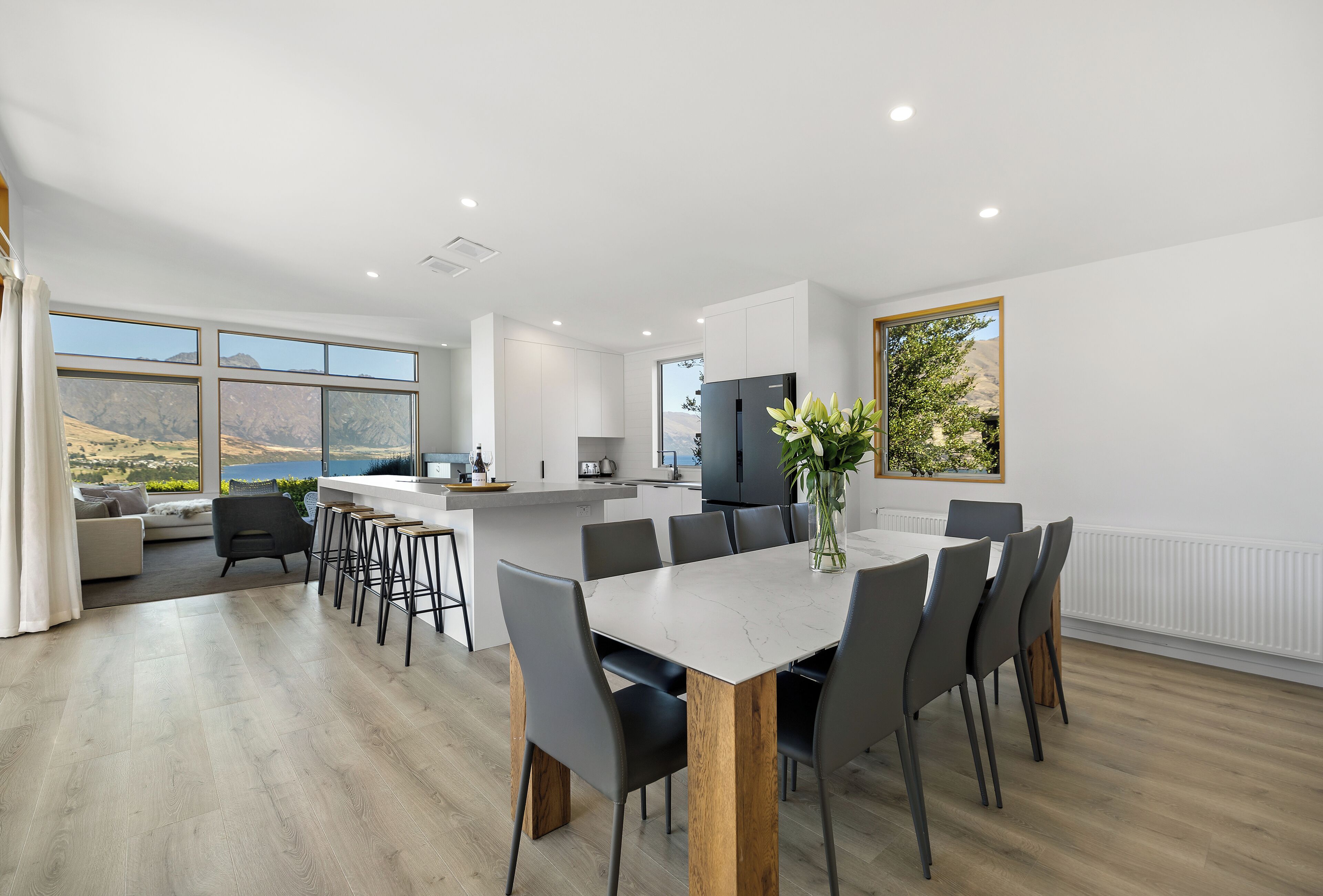 Une cuisine moderne dotée d’un grand îlot central, de meubles blancs et offrant une vue sur l’extérieur.