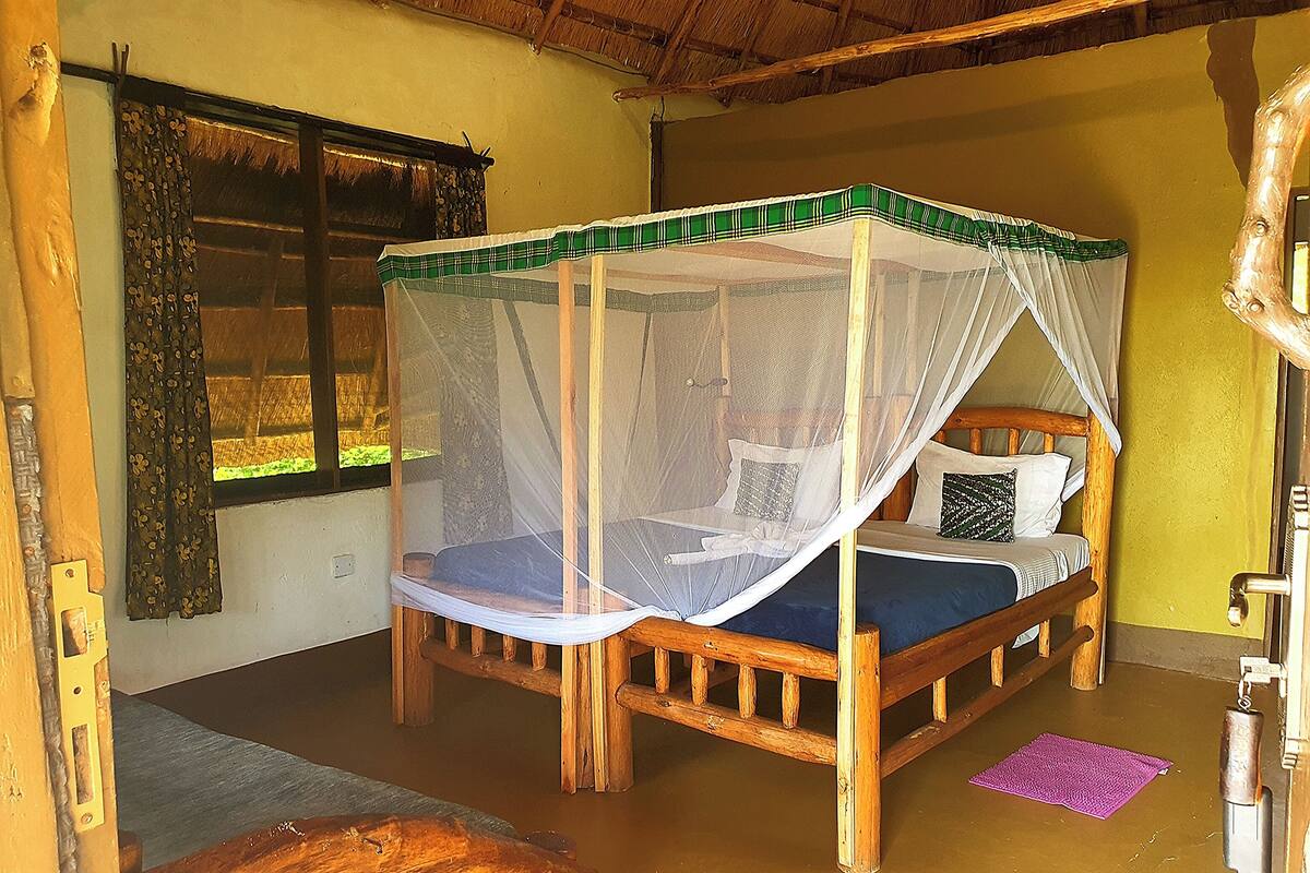 A wooden bed with a canopy, a window with curtains, and a wooden chair.
