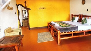 A room with a bed, a woven chair, a small table, and a mosquito net over the bed. - Hornbill Bush Lodge (Pakwach)