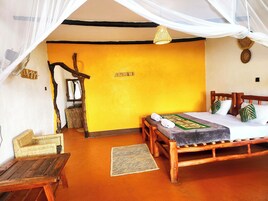 Una habitación con una cama, una silla de mimbre, una mesita y un mosquitero sobre la cama.