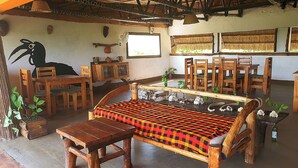 A rustic room with a wooden bench, a dining table with chairs, and a thatched roof. - Hornbill Bush Lodge (Pakwach)