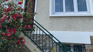 A two-story house with a beige exterior, a brown door, and a window with white frames. - Séjour en Pavillon Proche des Transports et des Évènements (Aulnay-sous-Bois)