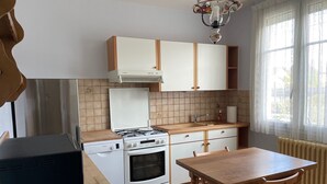 A compact kitchen with a stove, oven, and a small sink. There is a wooden table and chairs, and a radiator near the window. - Séjour en Pavillon Proche des Transports et des Évènements (Aulnay-sous-Bois)