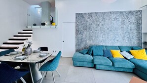 A modern living room with a teal sofa, a dining area with a marble table, and a staircase with a glass railing. - YourHome - AC Luxury House (Meta)