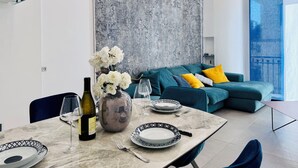 A modern living room with a teal sofa, a large abstract wall, and a dining area with a marble table set for a meal. - YourHome - AC Luxury House (Meta)