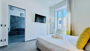 A modern hotel room with a large bed, a flat-screen TV mounted on the wall, a window with curtains, and a view of the outside. - YourHome - AC Luxury House (Meta)