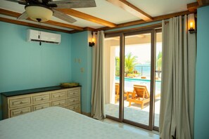 Ein Schlafzimmer mit Bett, Kommode, Klimaanlage und einer Glastür zum Poolbereich.