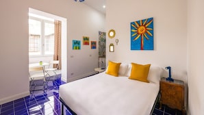 Une chambre d’hôtel avec un grand lit, un bureau et une chaise. Les murs sont ornés de tableaux et il y a une fenêtre avec des rideaux.
