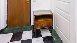 Un couloir avec une porte en bois, une petite armoire en bois, un téléphone blanc fixé au mur et une porte blanche.