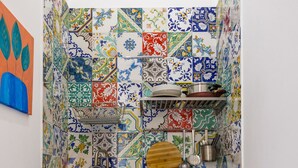 Une cuisine compacte avec des carreaux de couleurs vives, un évier, un petit réfrigérateur et une planche à découper en bois.