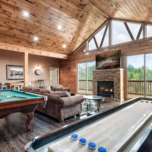 A pool table, a fireplace, and a large window overlooking a deck.