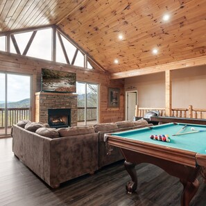 A cozy room with a pool table, a fireplace, and a large window overlooking a scenic view.