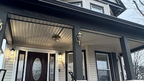 A two-story house with a dark front door, a covered porch, and a brick column.
