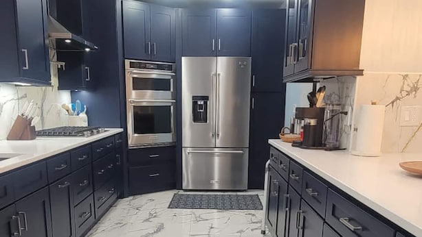 A modern kitchen with dark cabinets, stainless steel appliances, and a marble floor.