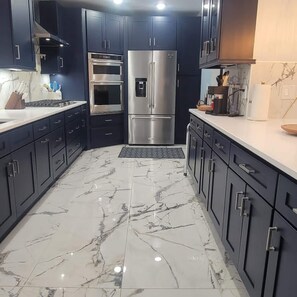 Una cocina moderna con armarios oscuros, electrodomésticos de acero inoxidable y piso de mármol.