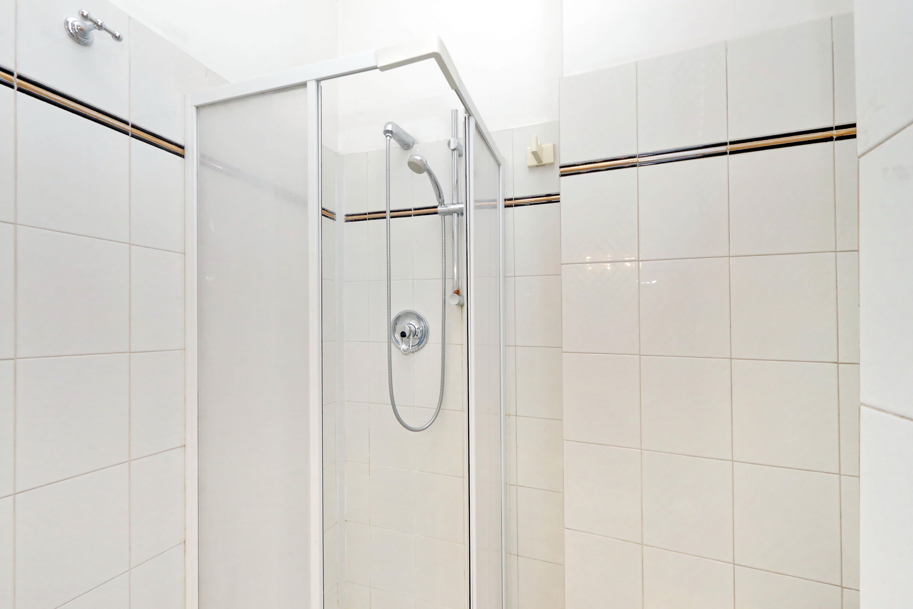 A glass-enclosed shower with a handheld showerhead and a wall-mounted faucet.