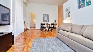 A modern living room with a sofa, TV, and a dining area with chairs and a table. - 4bnb - Lante Apartment (Rome)