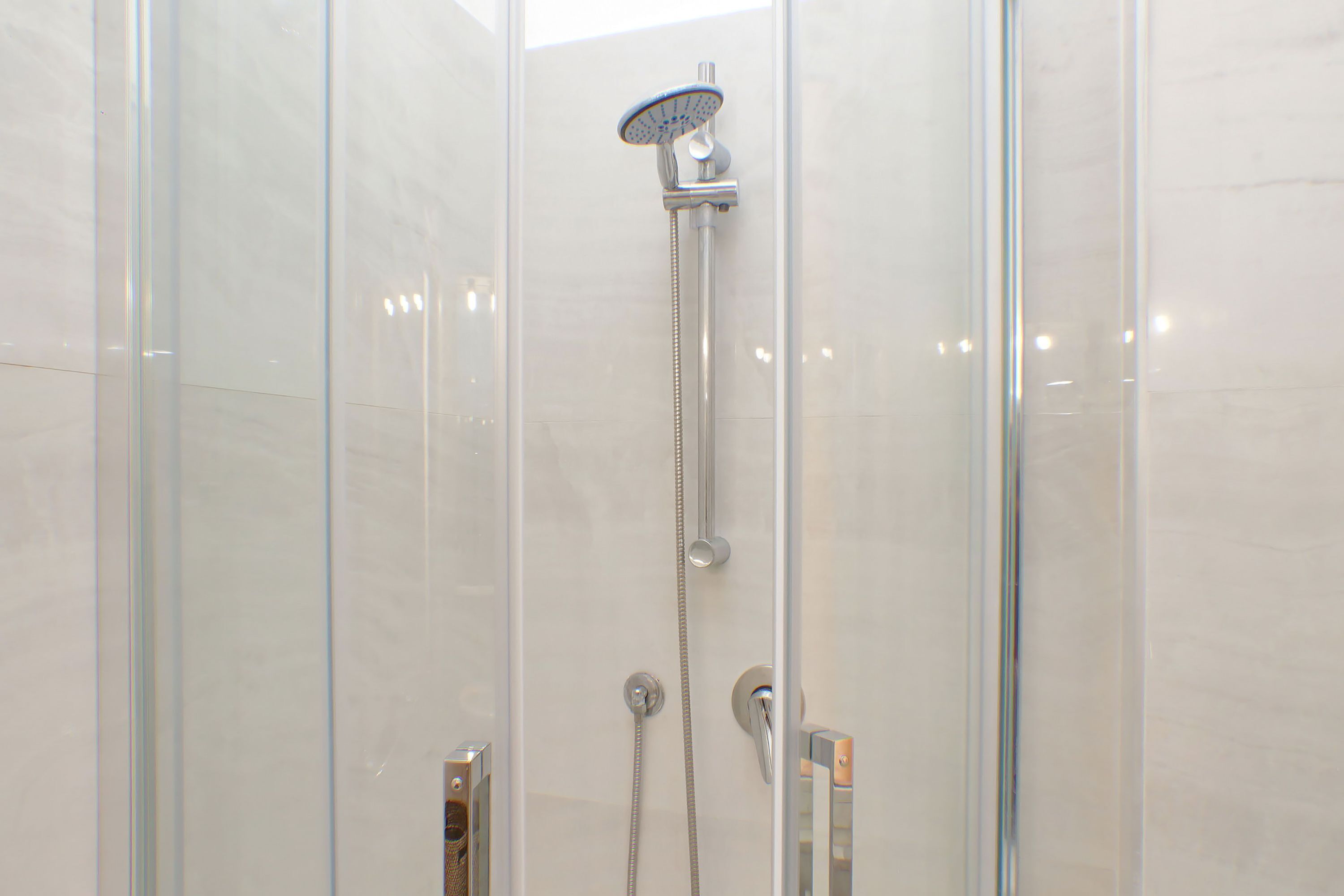 Une cabine de douche fermée par des parois en verre, dotée d’un pommeau de douche à main et d’un robinet mural.