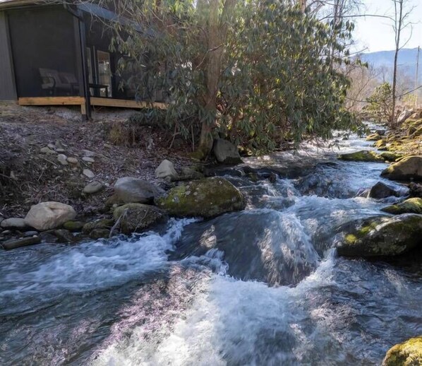 A stream flowing over rocks with a wooden structure nearby.