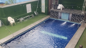 Une piscine avec une terrasse carrelée, entourée de gazon synthétique. On y trouve des chaises et un petit coin bar avec un comptoir en marbre.
