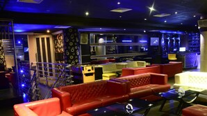 Un espace bar avec des canapés en cuir rouge, un canapé blanc et un comptoir de bar doté d’étagères.