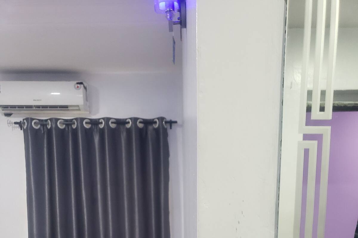 A small, dimly lit room with a single bed, a curtain, and a wall-mounted air conditioner.
