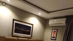 Une chambre d’hôtel avec un grand lit, deux tables de chevet, une petite table, un tableau encadré au mur et un appareil de climatisation.