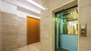 Un ascensor moderno con pantalla digital, suelo de baldosas de mármol y una puerta de madera en el pasillo.
