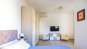 Una habitación de hotel moderna con una cama grande, un televisor de pantalla plana, dos sillones, un armario de madera y un aire acondicionado instalado en la pared.